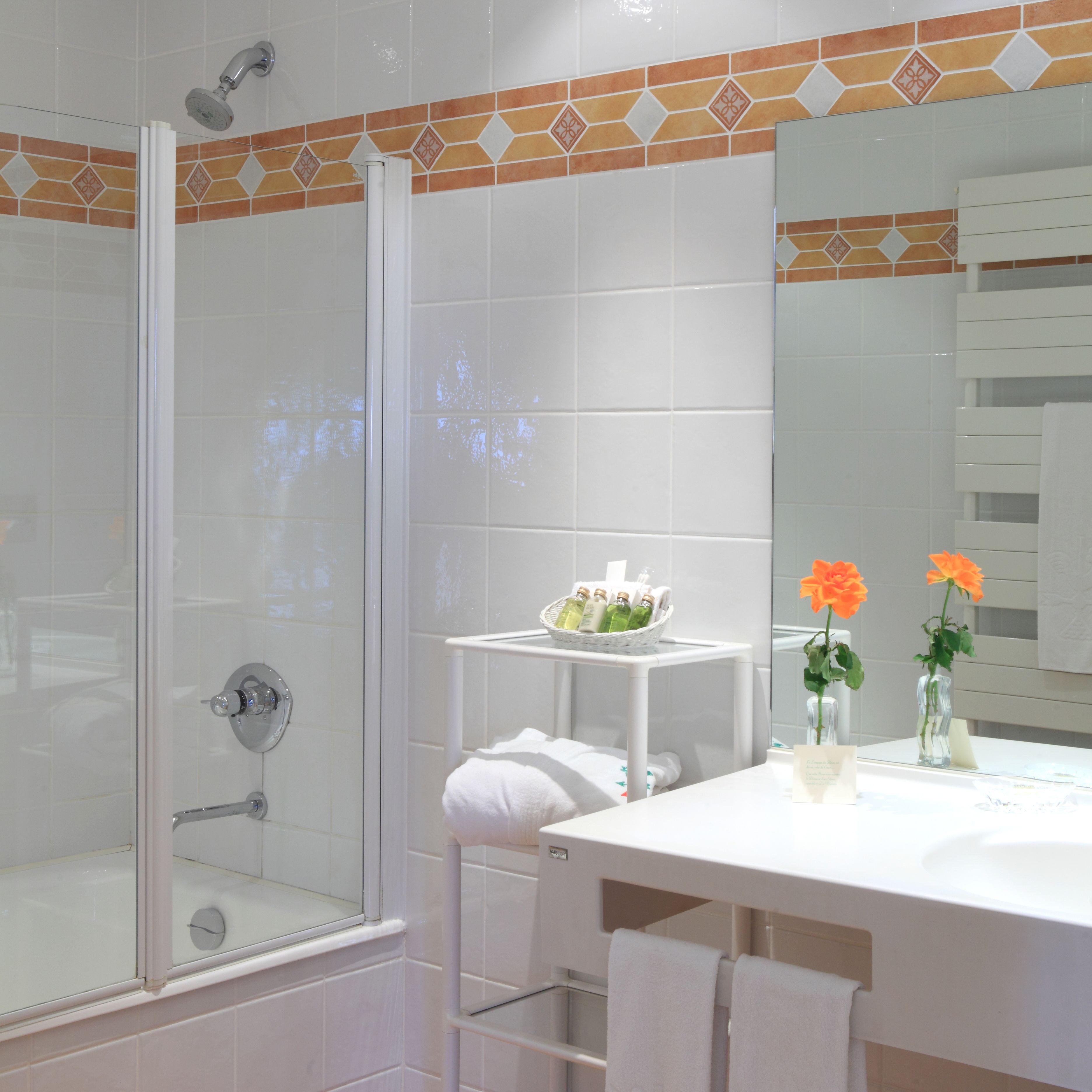Un baño moderno con cabina de ducha de vidrio, un lavamanos blanco con espejo y una mesita con artículos de aseo.
