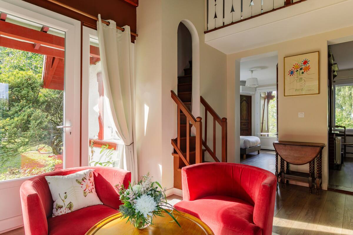 A living room with a red sofa, a wooden coffee table, and a view of a garden through a large window.