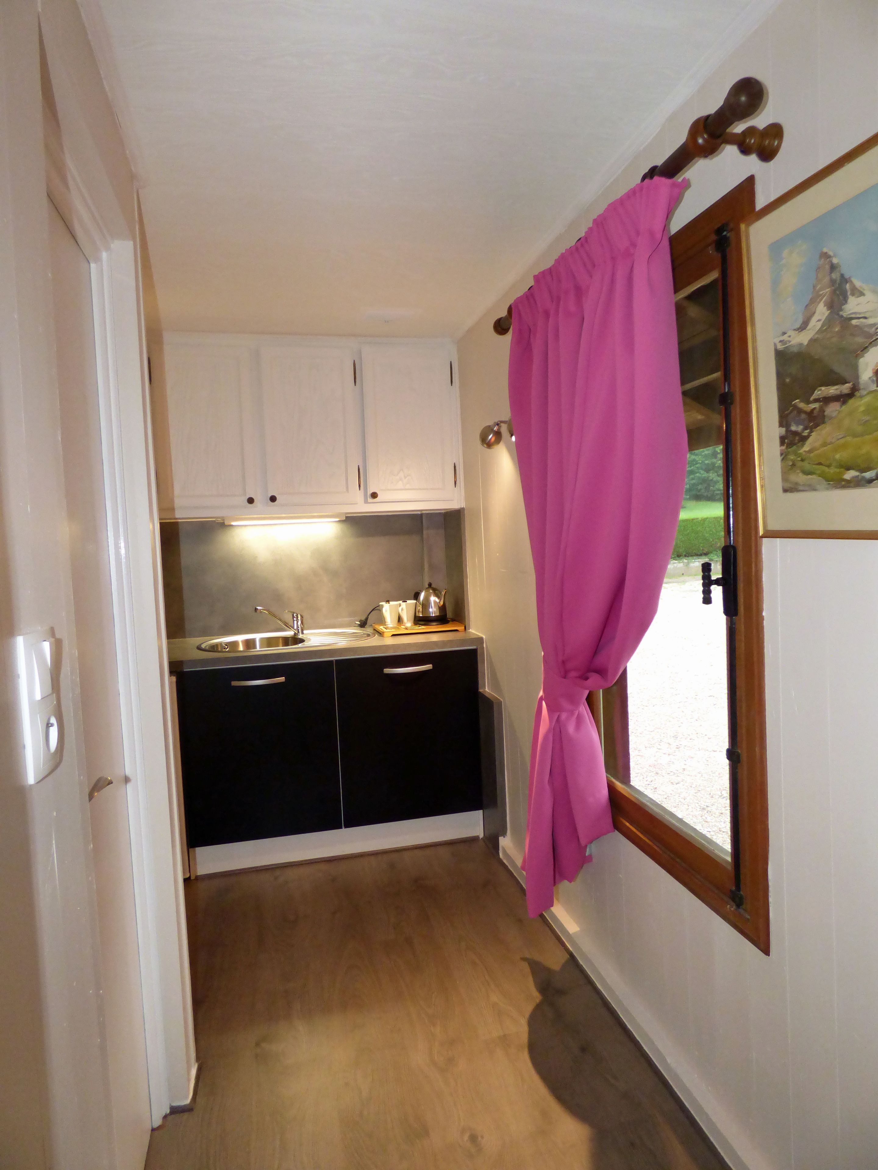 A kitchen with white cabinets, a black countertop, and a window with a pink curtain.