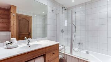 Ein modernes Badezimmer mit einem Holzbadezimmerhocker, einem großen Spiegel, einer Duschkabine aus Glas und einem weiß gefliesten Duschbereich.