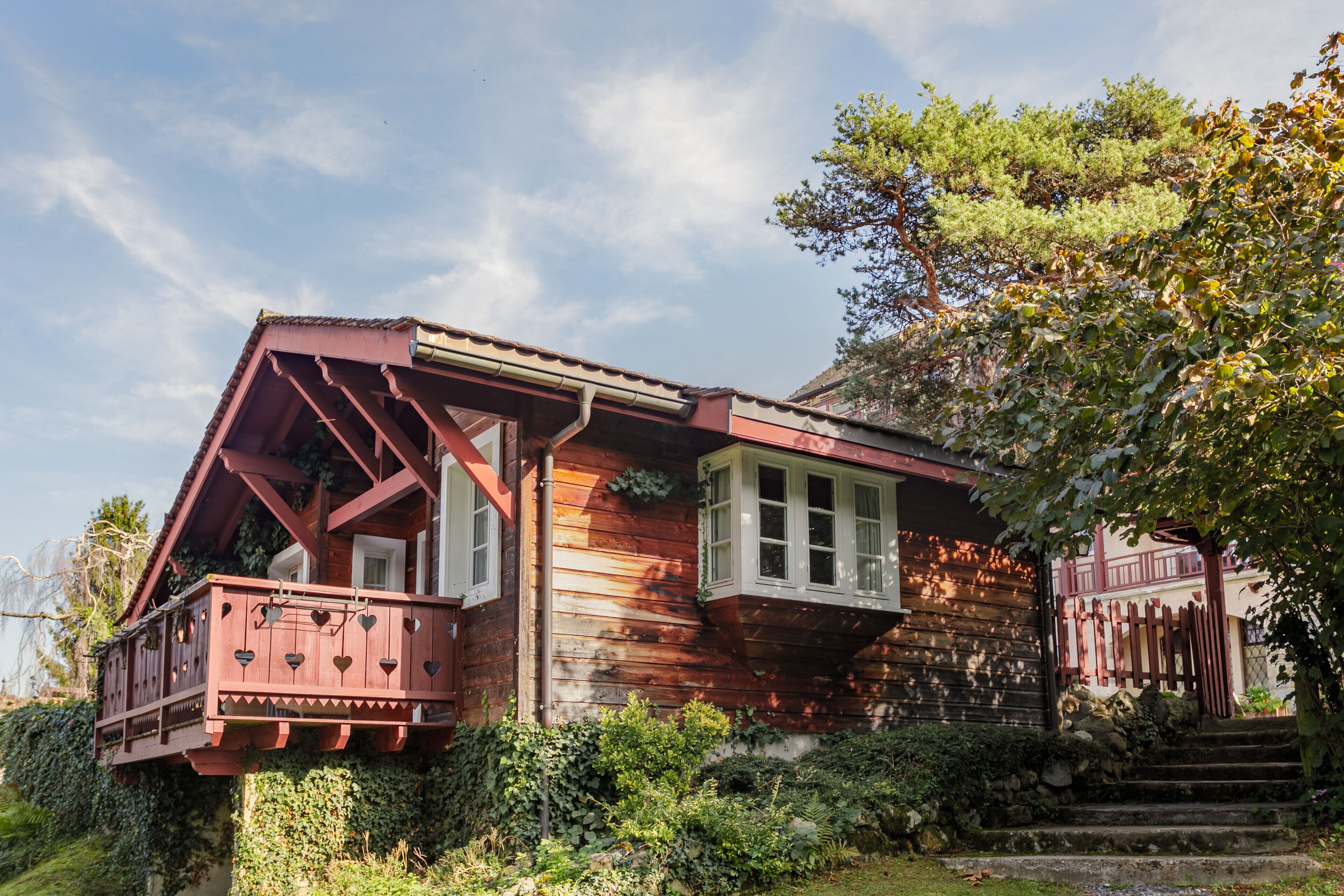 A wooden house with a balcony, steps leading up to the entrance, and a garden area.
