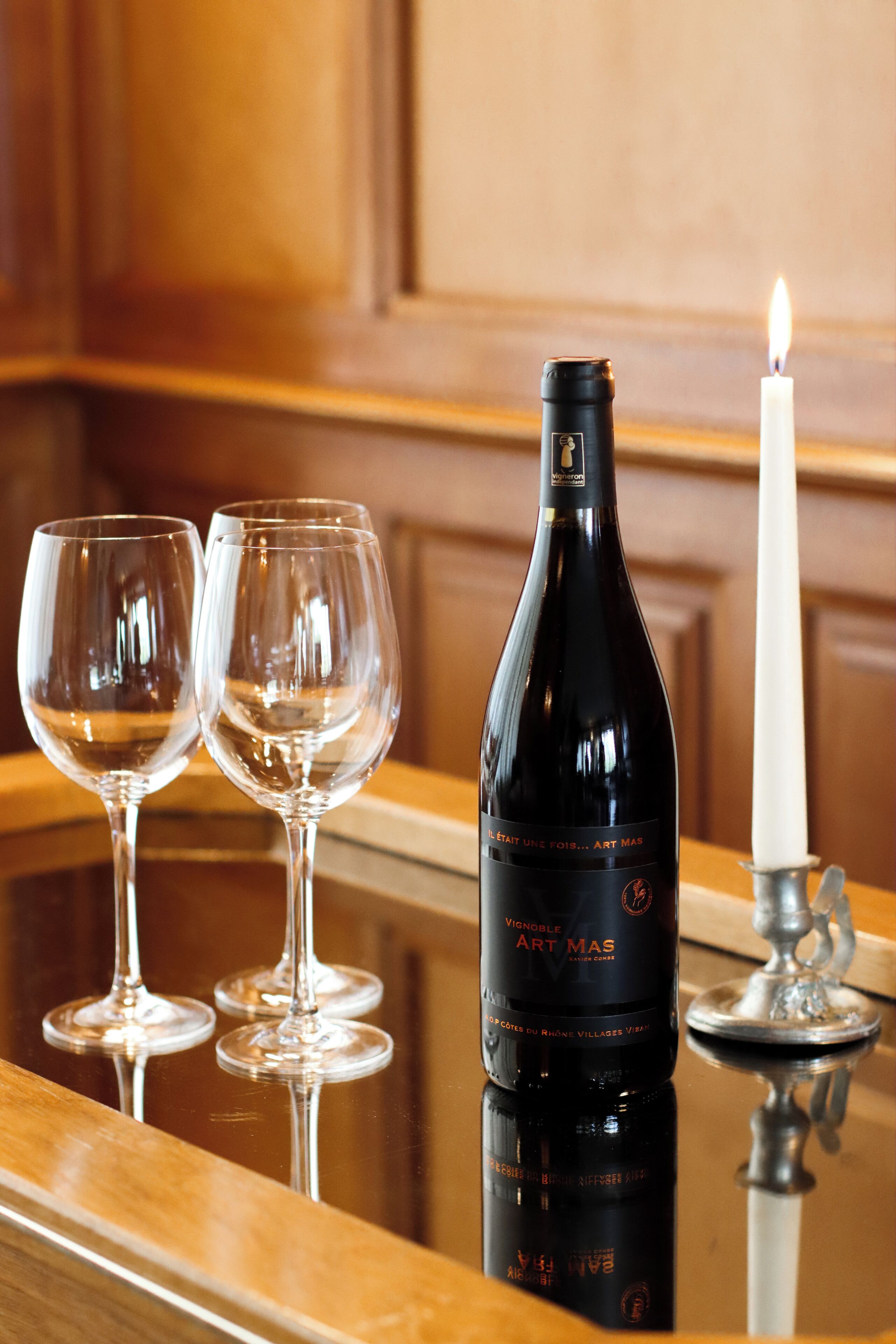 A bottle of wine, two glasses, and a lit candle on a reflective surface.