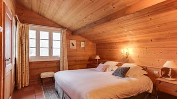 Un dormitorio de cabaña de madera con una cama grande, dos mesitas de noche, un banco y una ventana con cortinas.