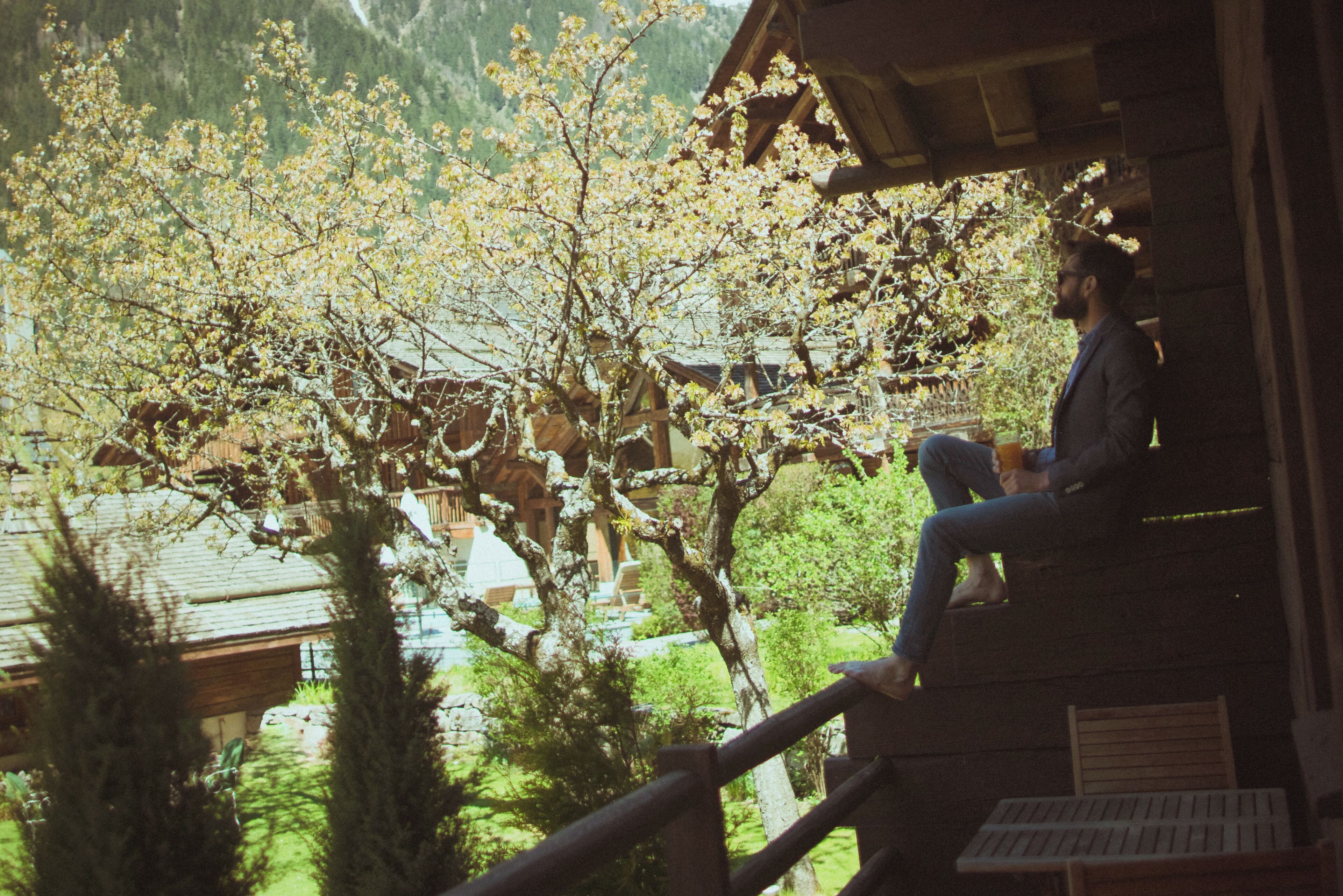 Una persona sentada en una terraza de madera con vistas a una montaña y árboles en flor.