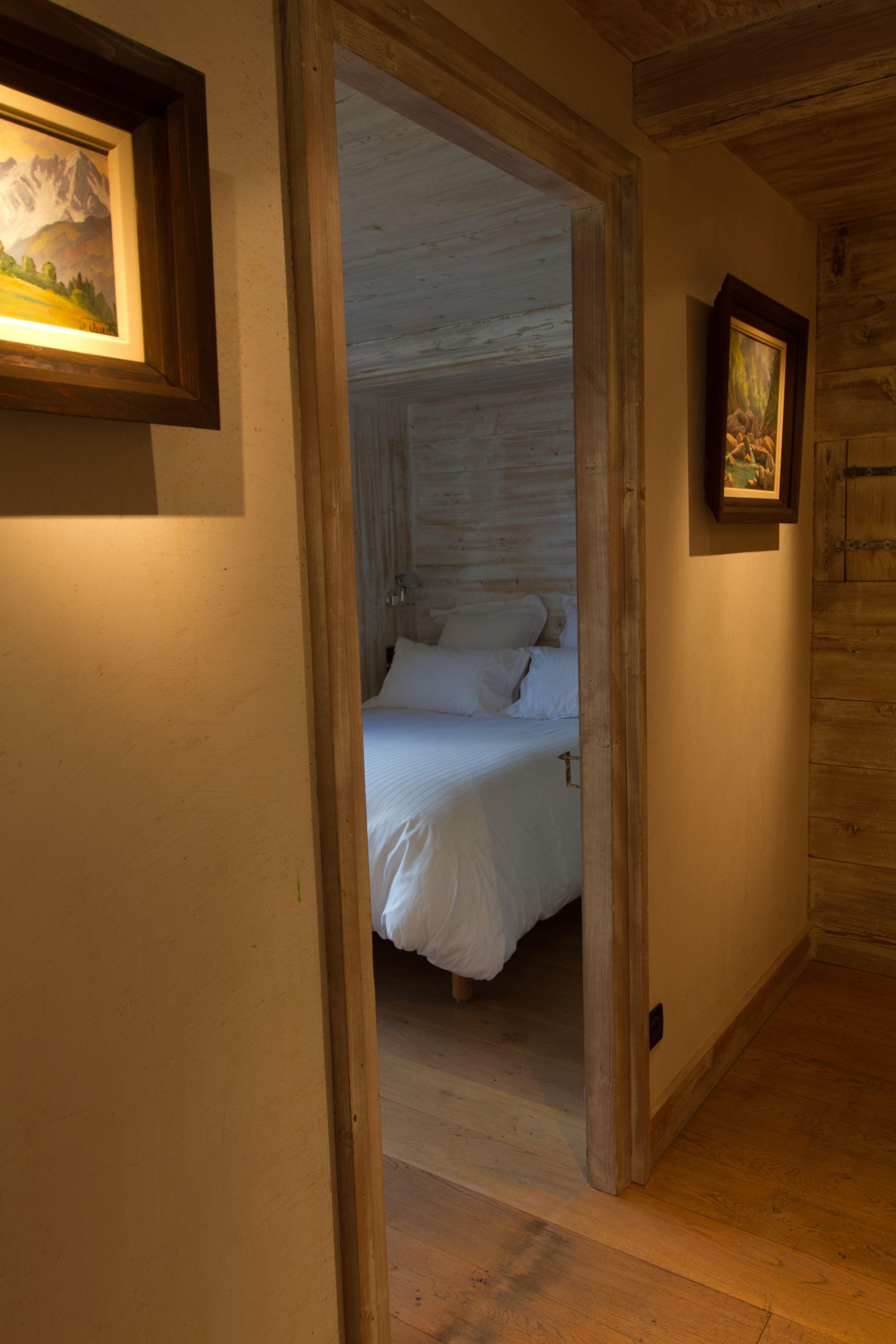 A narrow hallway leading to a bedroom with a bed and a framed picture on the wall.