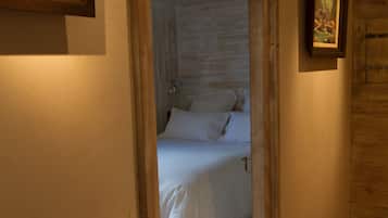 A narrow hallway leading to a bedroom with a bed and a framed picture on the wall.