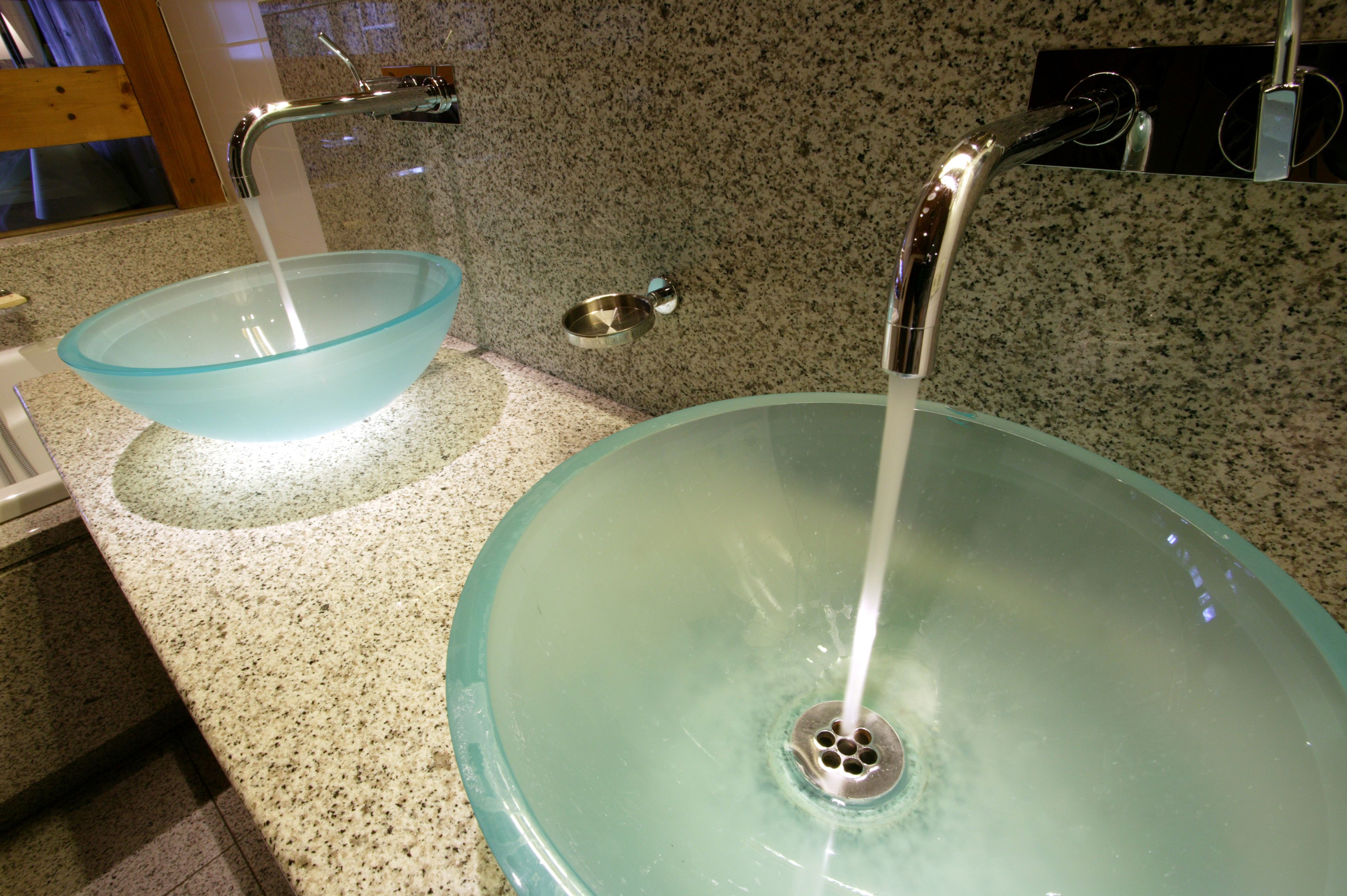 A bathroom with a granite countertop, a glass bowl sink, and a modern faucet.