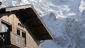 A wooden building with a balcony, set against a backdrop of snow-covered mountains. - Le Hameau Albert 1er - Relais & Châteaux (Chamonix-Mont-Blanc)