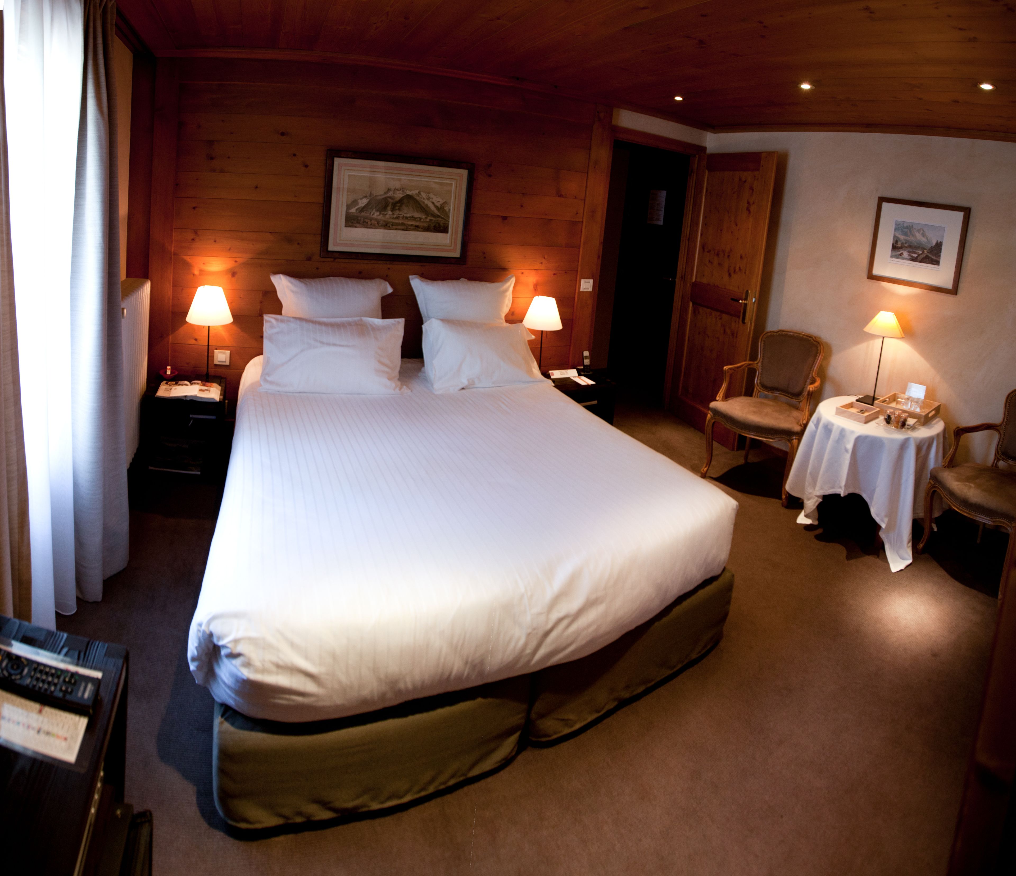A large bed with white linens, two bedside tables with lamps, a chair, a small table with a lamp, and a framed picture on the wall.
