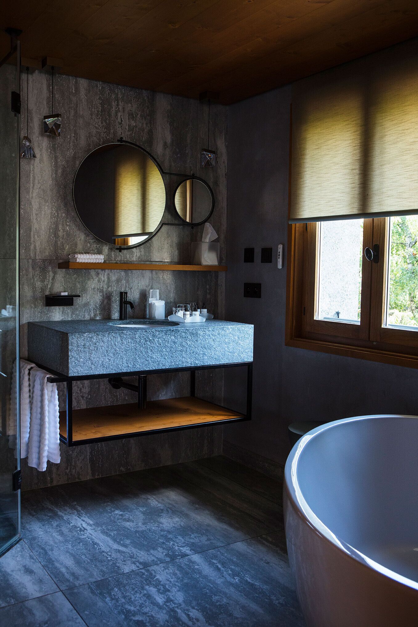 Un baño moderno con una bañera grande, un lavamanos de encimera de granito, un estante de madera y un espejo amplio.