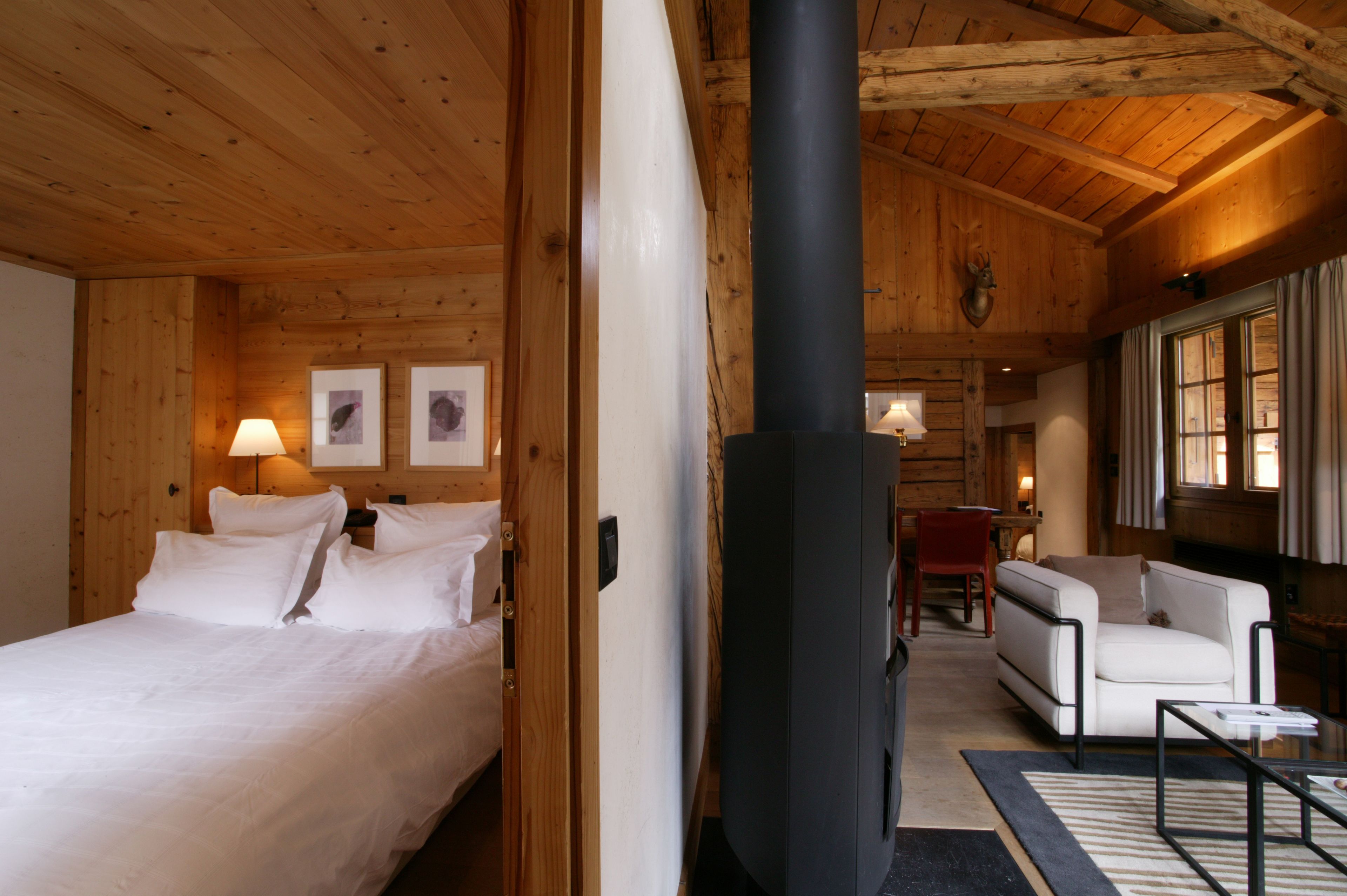 Interior de cabana de madeira com cama, sofá, lareira e quadros nas paredes.