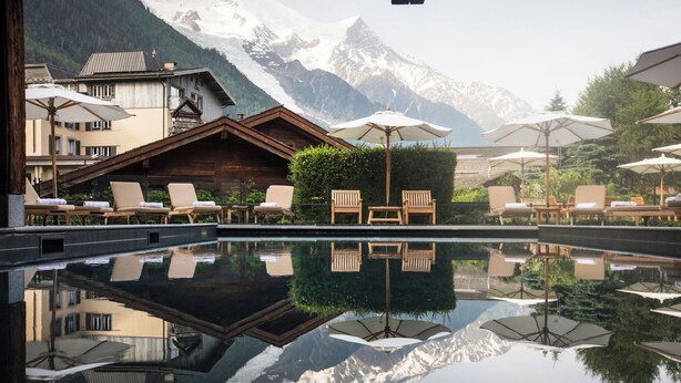 A pool with lounge chairs and umbrellas, reflecting a mountain backdrop. - Le Hameau Albert 1er - Relais & Châteaux (Chamonix-Mont-Blanc)