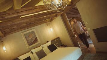 Un dormitorio con techo de madera, una cama con almohadas blancas y oscuras, un cuadro en la pared y una lámpara colgante.