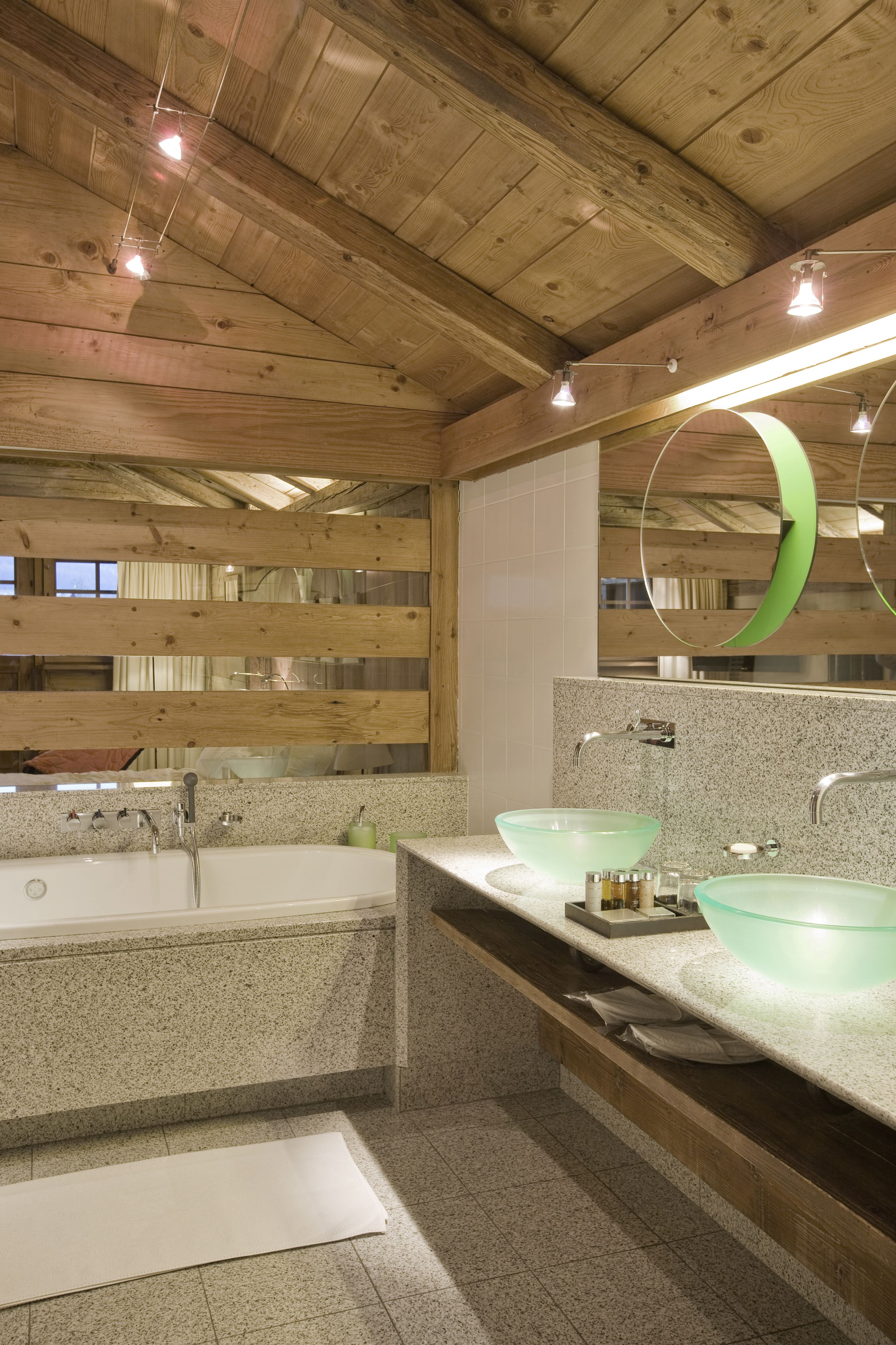 A wooden cabin bathroom with a large bathtub, two glass sinks, and a mirror with a green frame.