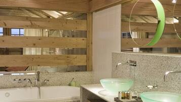 A wooden cabin bathroom with a large bathtub, two glass sinks, and a mirror with a green frame.