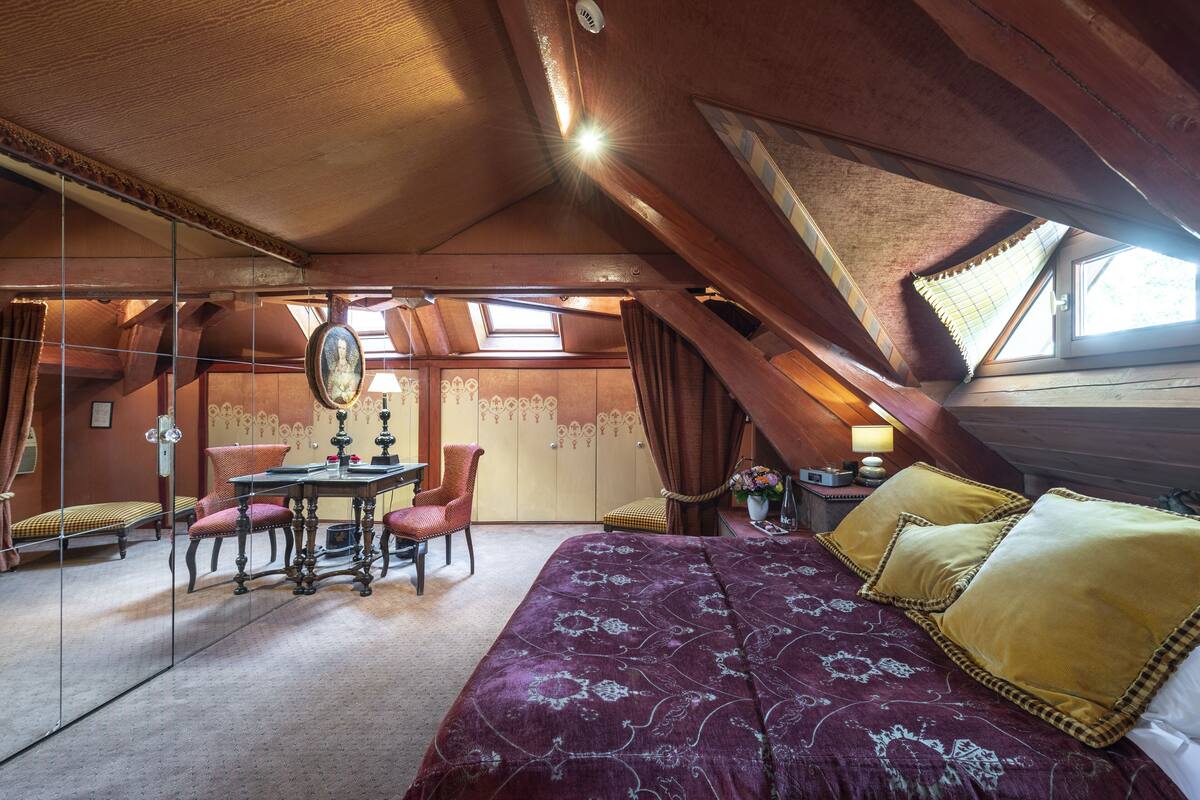 Un dormitorio acogedor en el ático, con una cama grande, una mesa de comedor y un espejo.