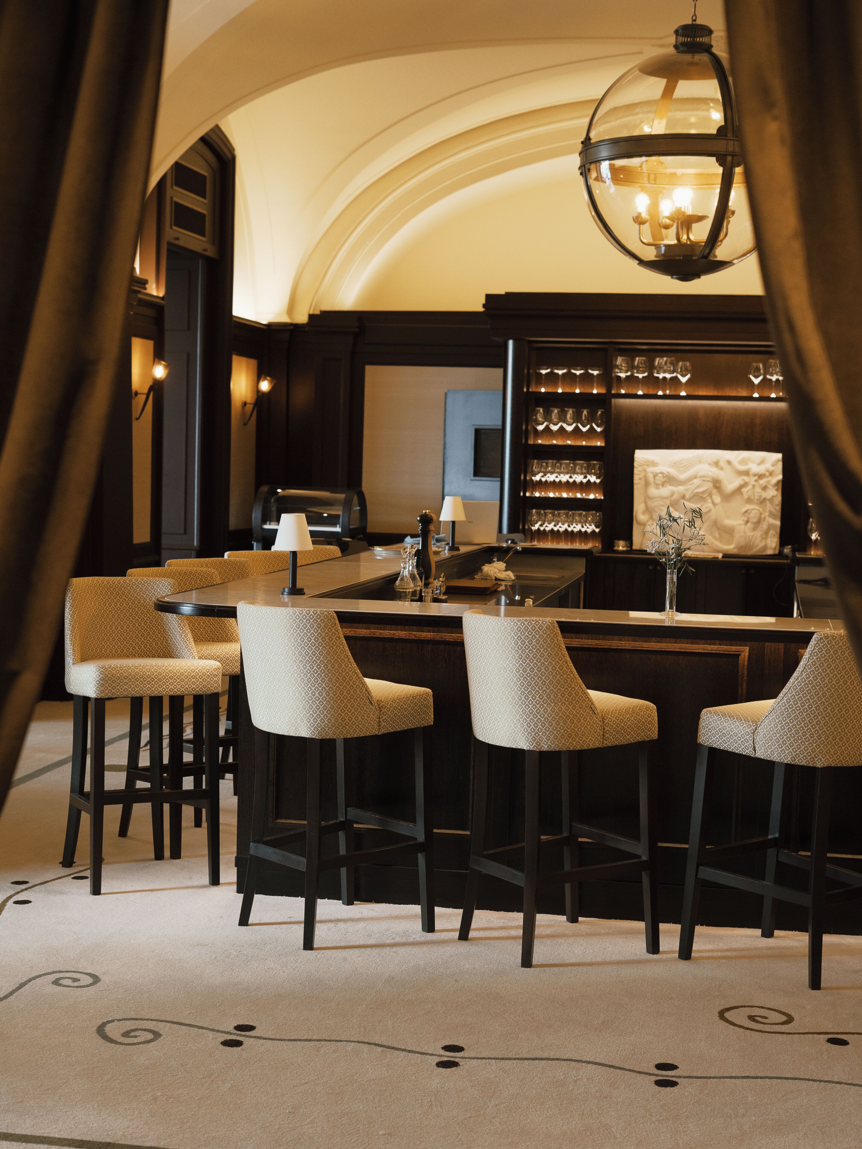 A bar area with a round table, bar stools, and a hanging light fixture.