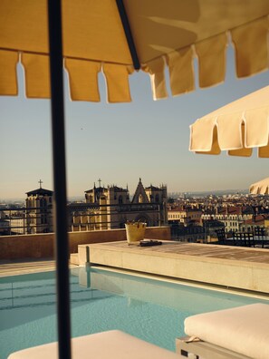 Una piscina en la azotea con vistas a edificios históricos, una silla de descanso y una sombrilla.