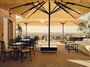 An outdoor patio with tables and chairs, umbrellas, and a city view.