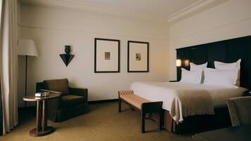 Habitación de hotel con cama, una silla, una mesita y dos cuadros en la pared.