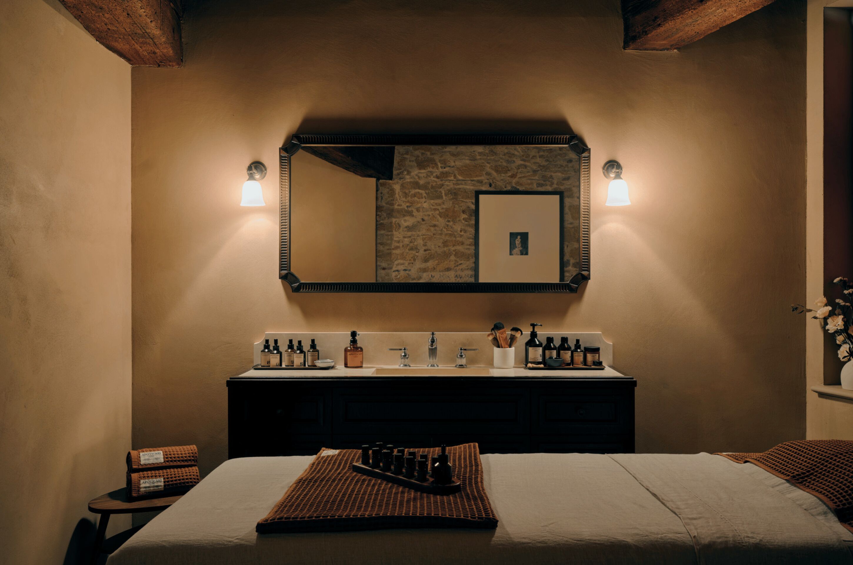 Une chambre d’hôtel avec un grand lit, une coiffeuse avec des articles de toilette, un miroir et un mur en pierre.