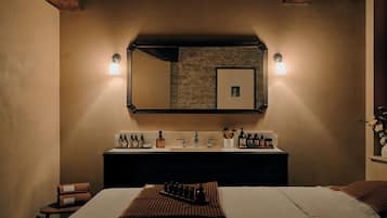 Une chambre d’hôtel avec un grand lit, une coiffeuse avec des articles de toilette, un miroir et un mur en pierre.