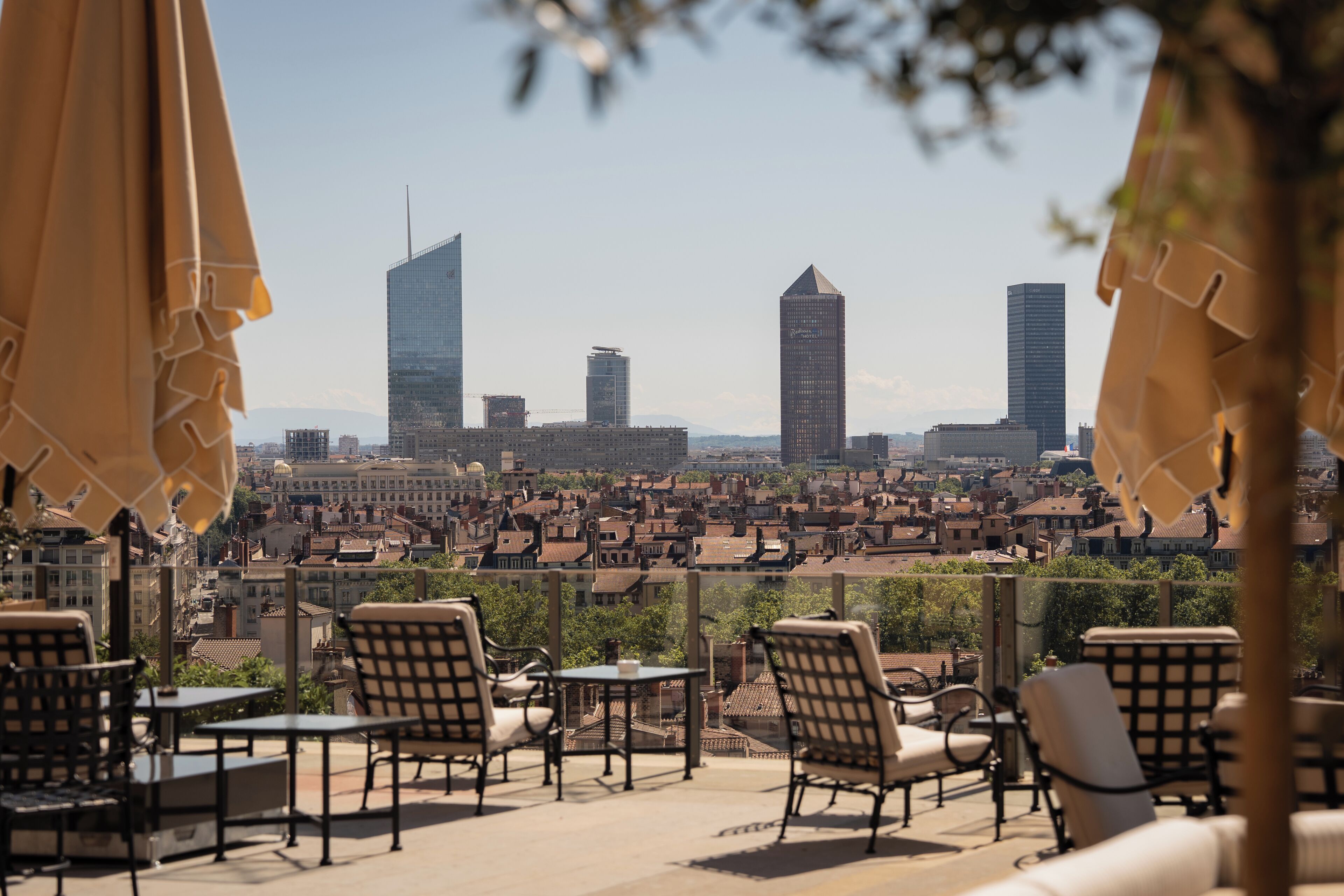A rooftop terrace with outdoor seating, a cityscape view, and modern buildings in the background.