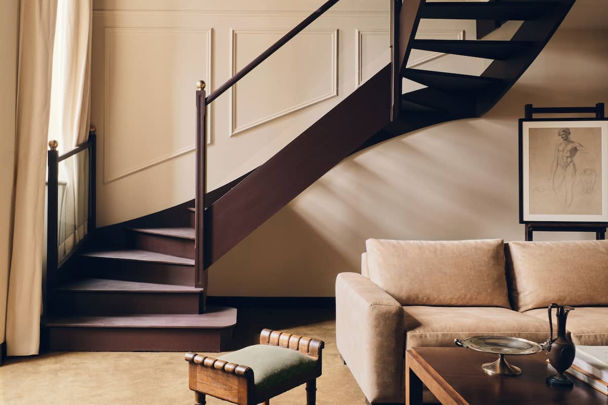 A staircase with wooden steps and a dark handrail, leading to a landing with a beige wall and a framed picture.