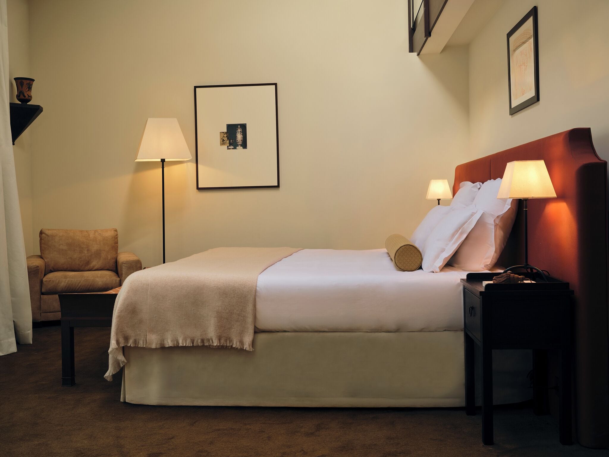 Habitación de hotel con una cama, dos mesitas de noche, una silla, una lámpara de pie y un cuadro colgado en la pared.