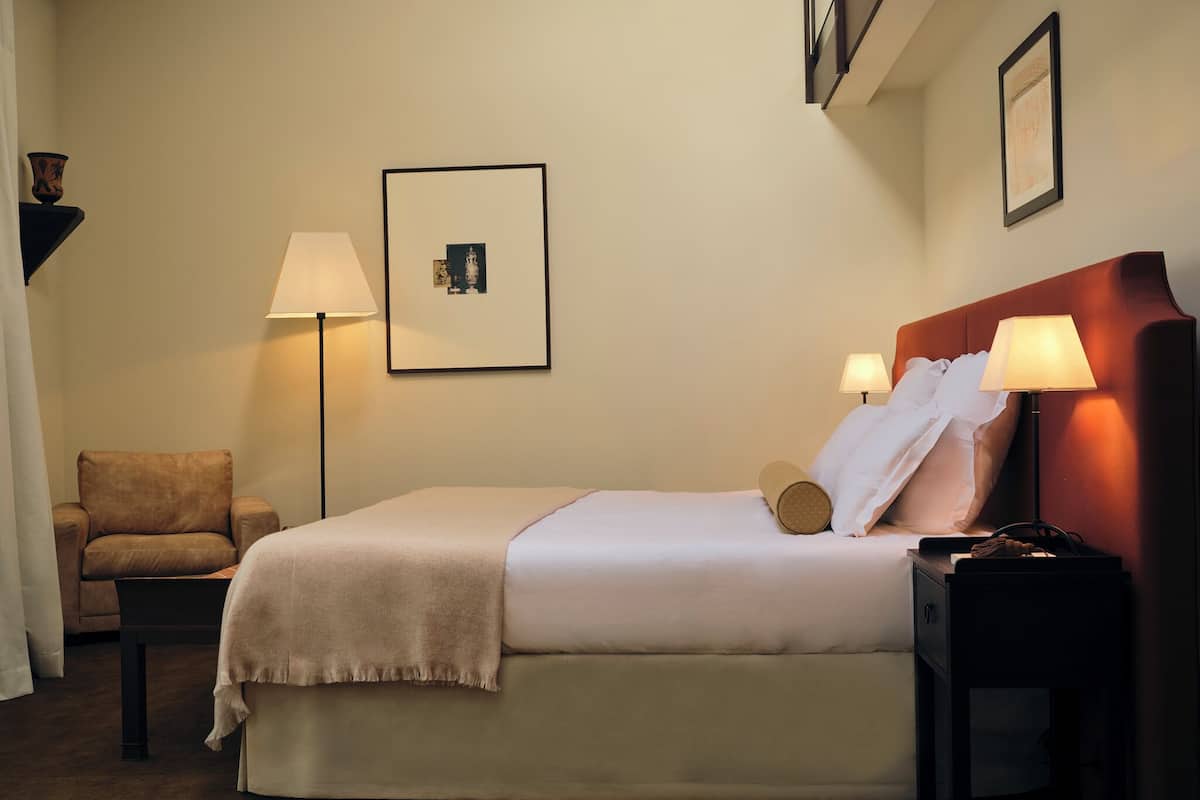 A hotel room with a bed, two bedside tables, a chair, a floor lamp, and a wall-mounted picture.