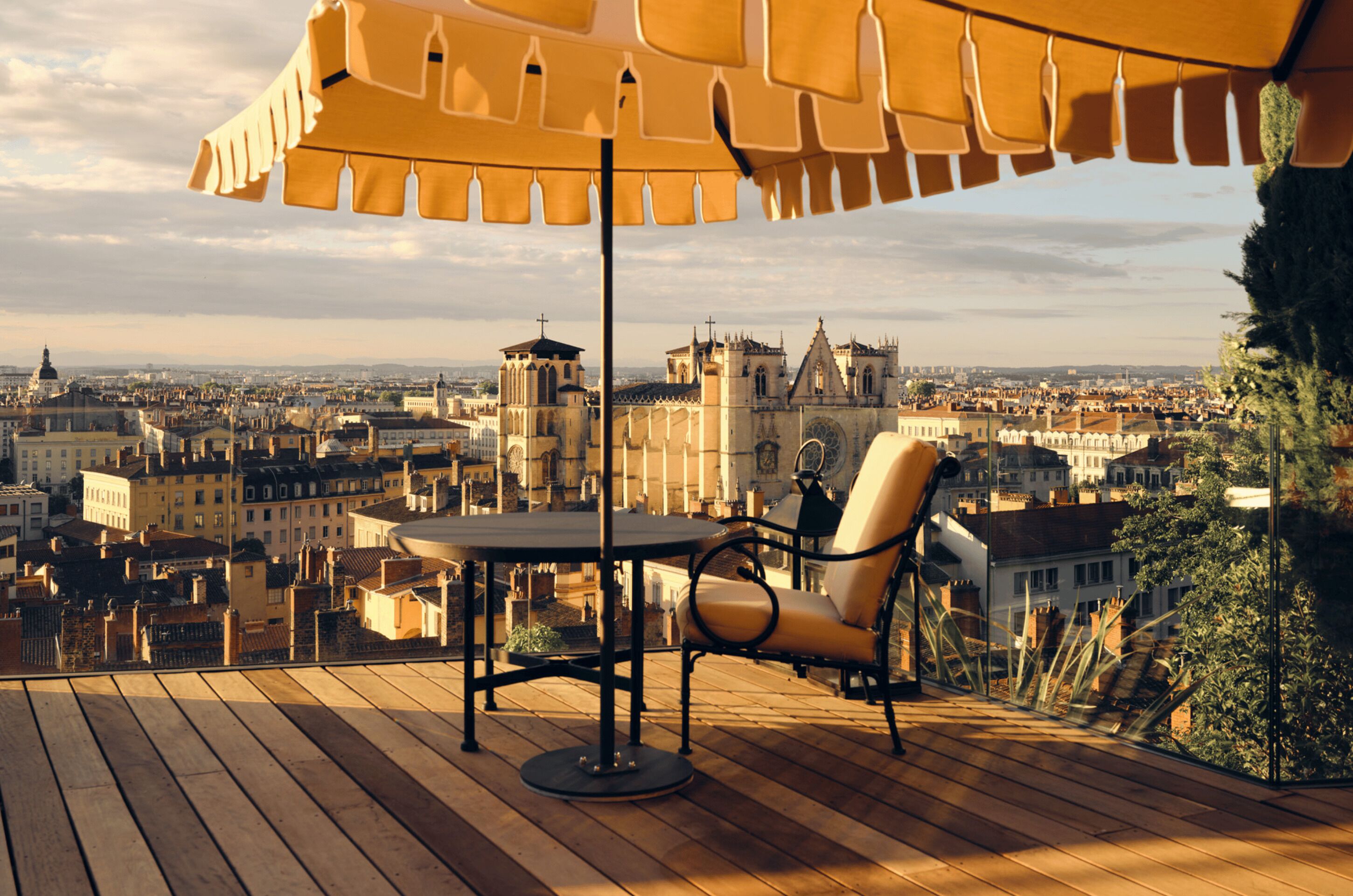A wooden deck with a table and chair, overlooking a cityscape with historic buildings.