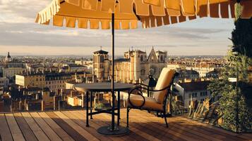 Une terrasse en bois avec une table et une chaise, offrant une vue sur le paysage urbain et ses bâtiments historiques.