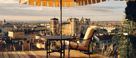 Terraza de madera con una mesa y una silla, con vista a un paisaje urbano con edificios históricos.