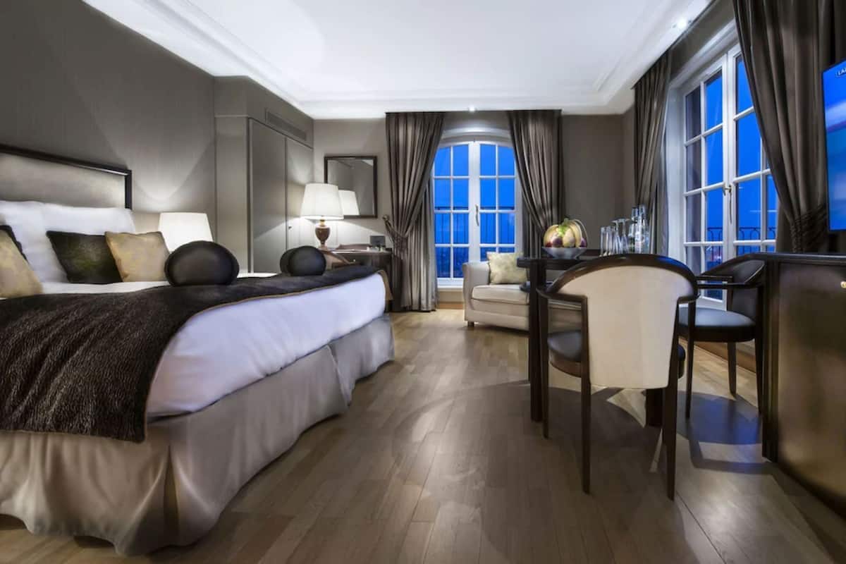 A hotel room with a large bed, a desk, a chair, and a view of the sky through the window.