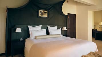 Habitación de hotel con una cama grande, dos mesitas de noche, una colcha oscura con dosel y un cuadro en la pared.