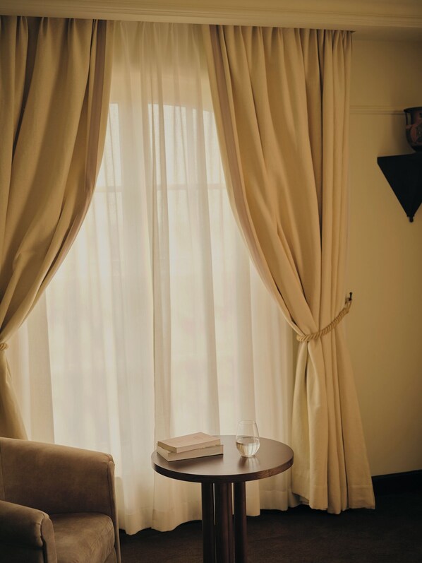 A room with a round table, a chair, and a window with curtains.