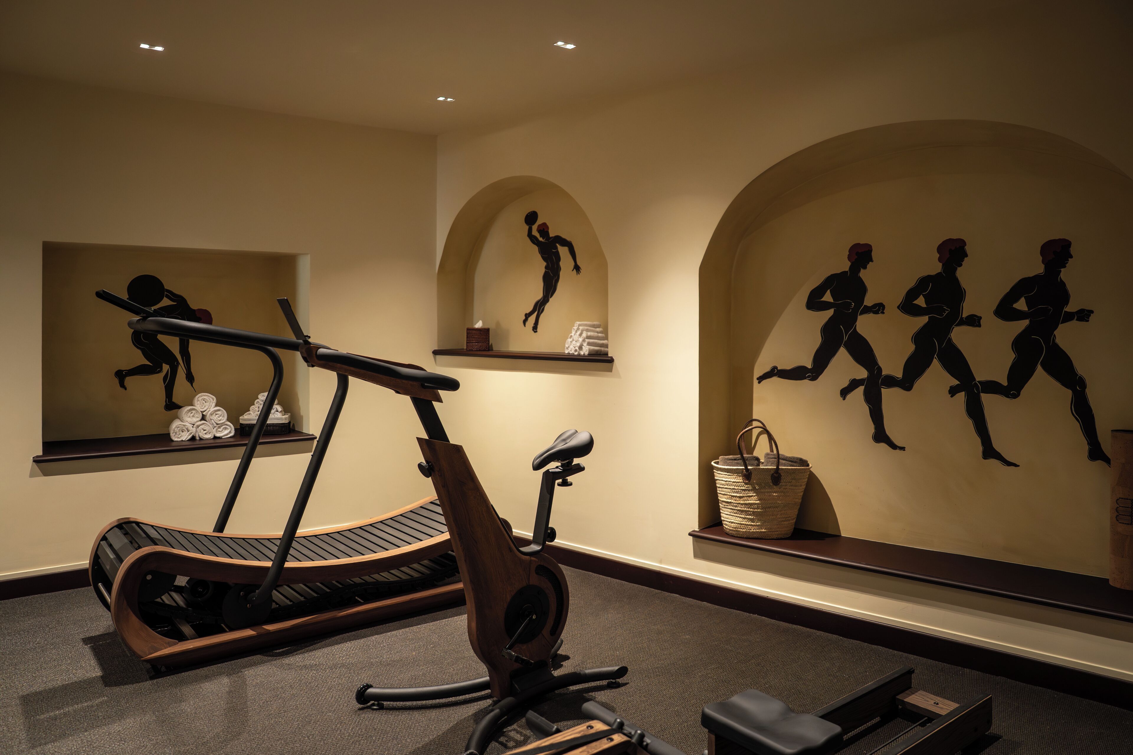 Une salle de sport équipée de matériel d’exercice, un mur orné de silhouettes de coureurs et une fenêtre avec des serviettes.