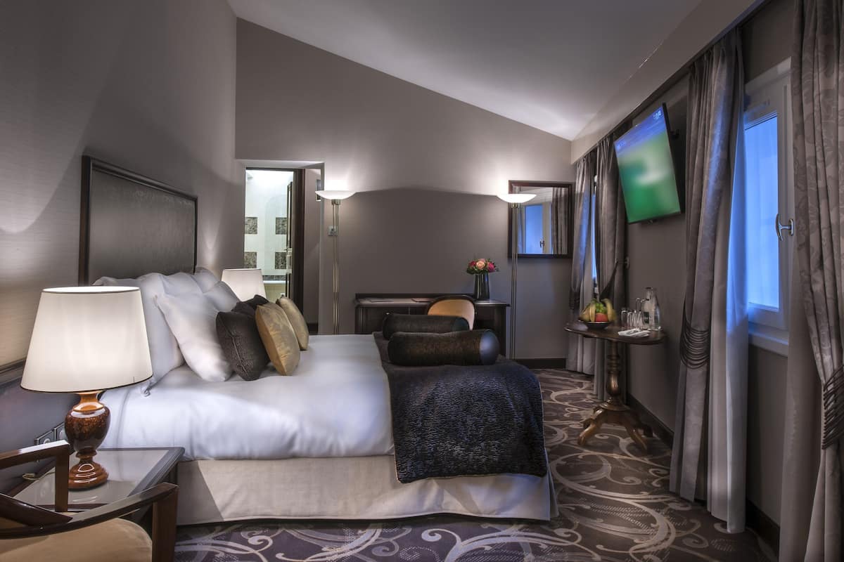 A hotel room with a bed, a desk, a TV, and a window with curtains.