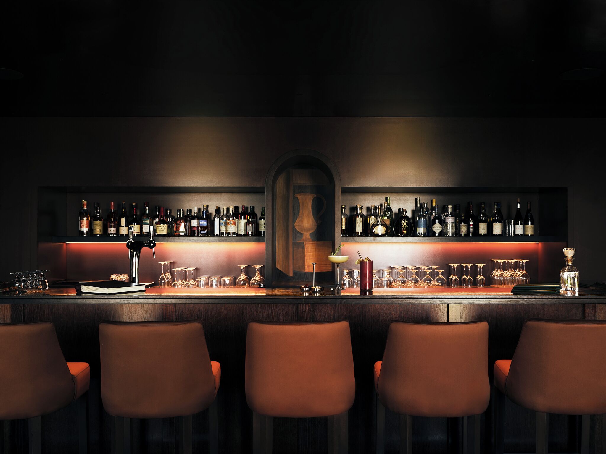 A bar with multiple shelves of bottles, glasses, and a central bar counter.