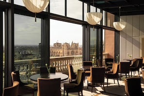 A high-rise hotel room with large windows, a round dining table, and modern chairs.