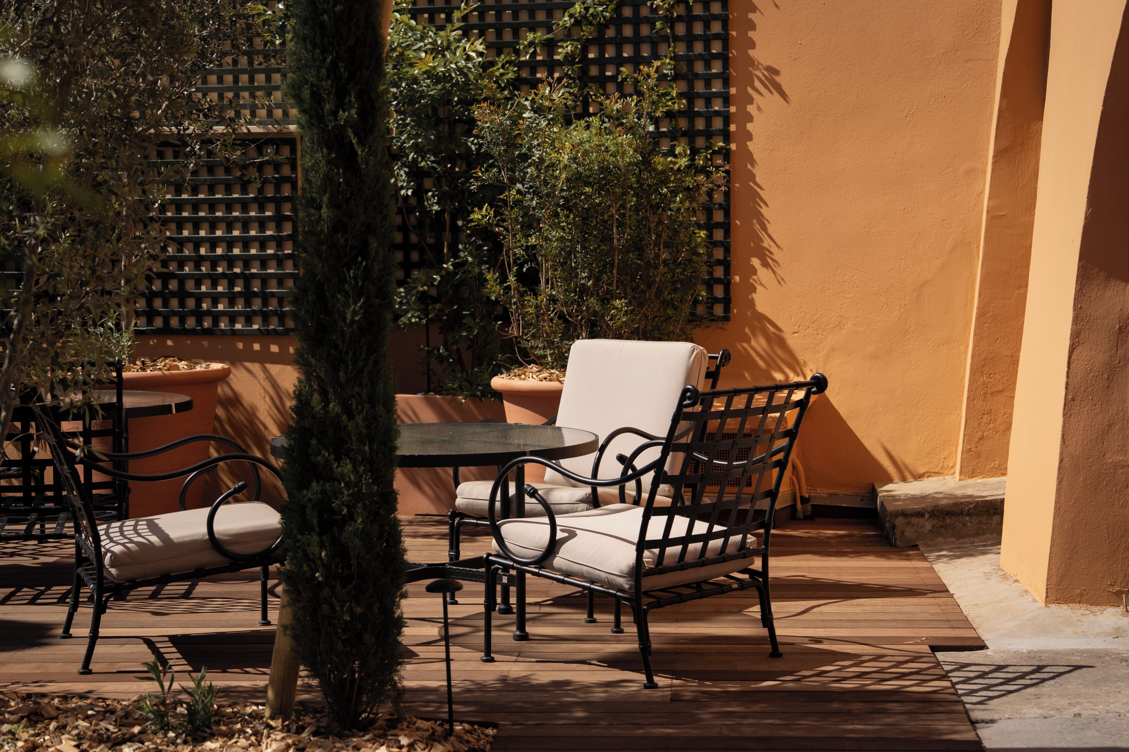An outdoor patio with a table and chairs, surrounded by plants and a lattice wall.