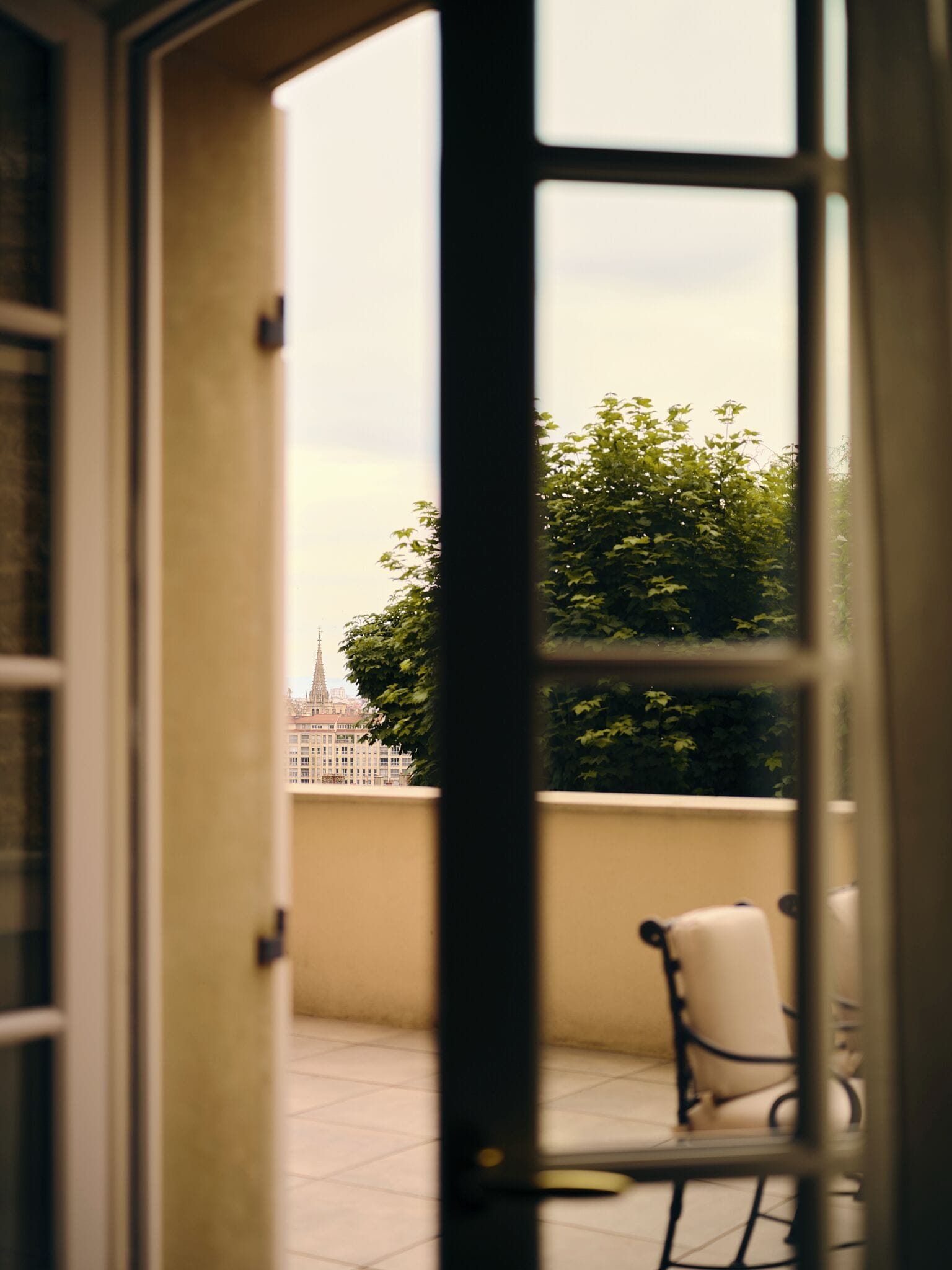 Una porta aperta con vista su un balcone, una sedia e un edificio sullo sfondo.