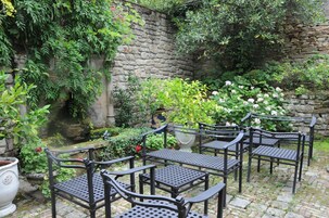 Un patio jardín con muros de piedra, plantas en macetas y sillas de metal.