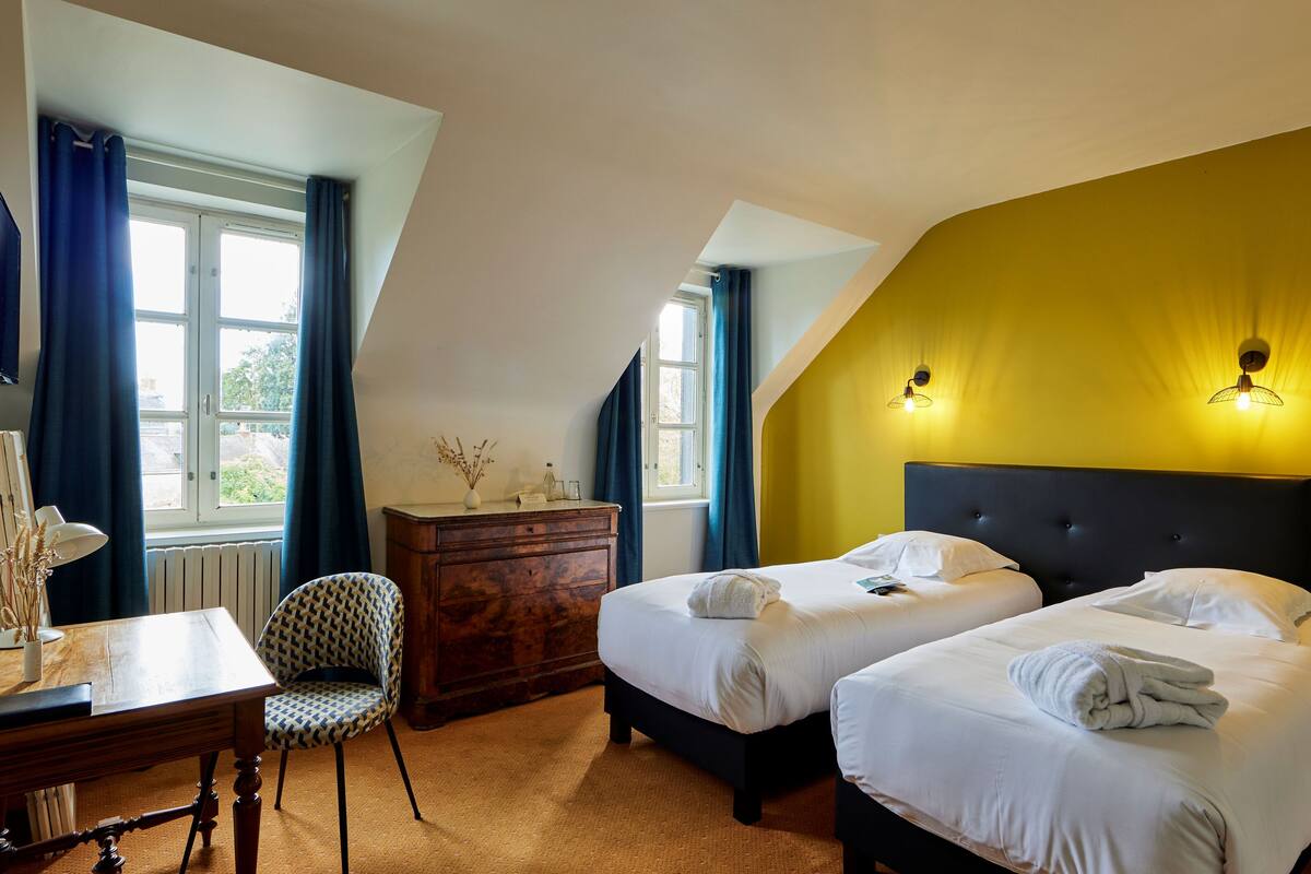 A room with two beds, a wooden dresser, a desk with a lamp, and a chair.