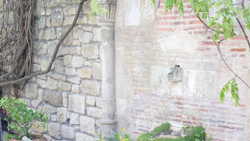 Muro de piedra con sección de ladrillo, vegetación exuberante y una maceta de piedra cubierta de musgo.