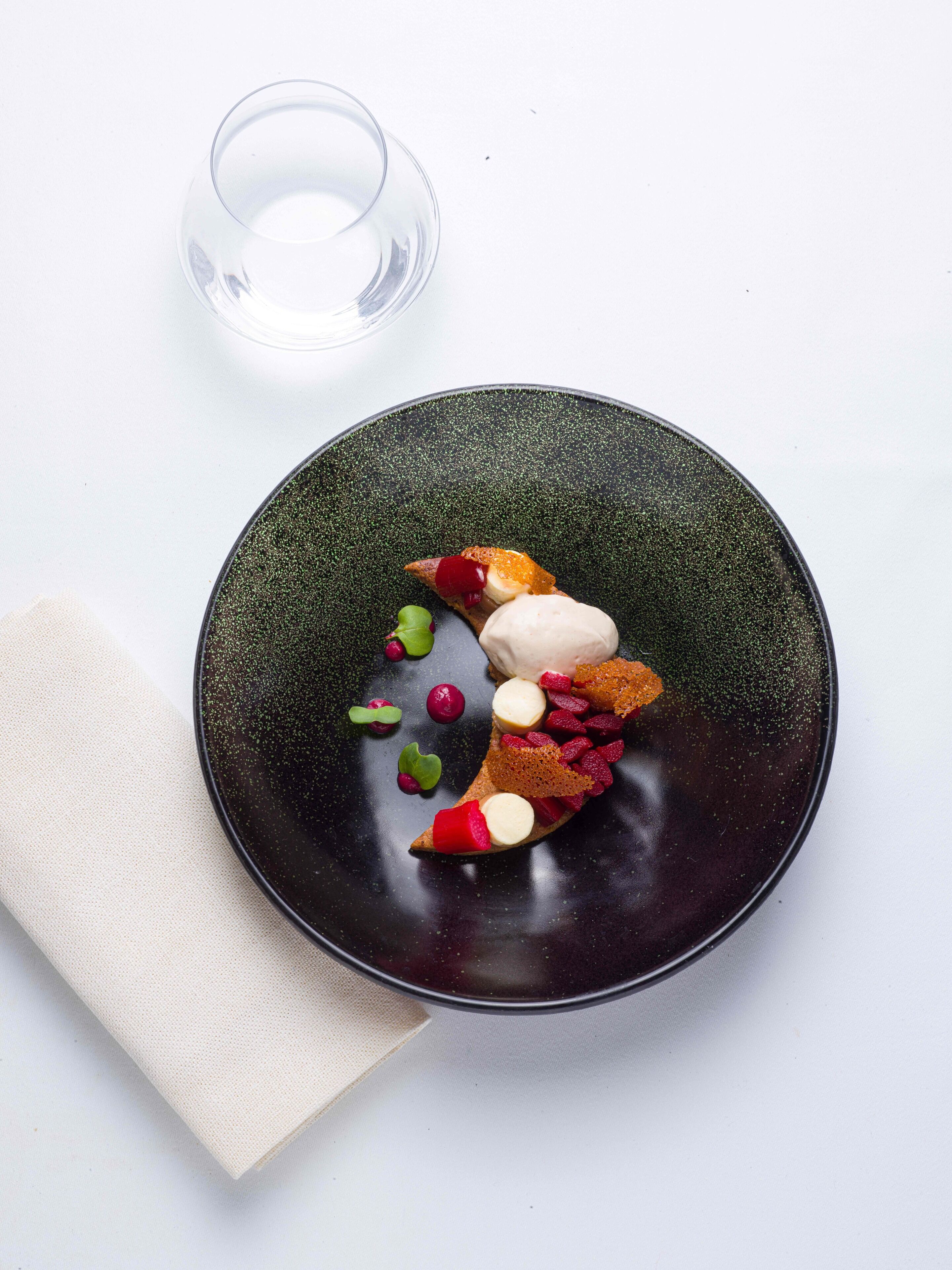 A plate with various food items and a glass of water on a white surface.