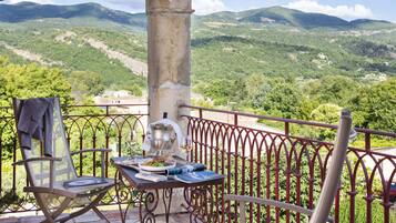A balcony with a table set for dining, a chair, and a view of a mountainous landscape.