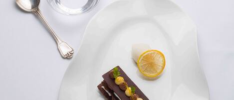 Ein weißer Teller mit Dessert, einem Löffel, einem Glas und einer Serviette auf weißer Oberfläche.