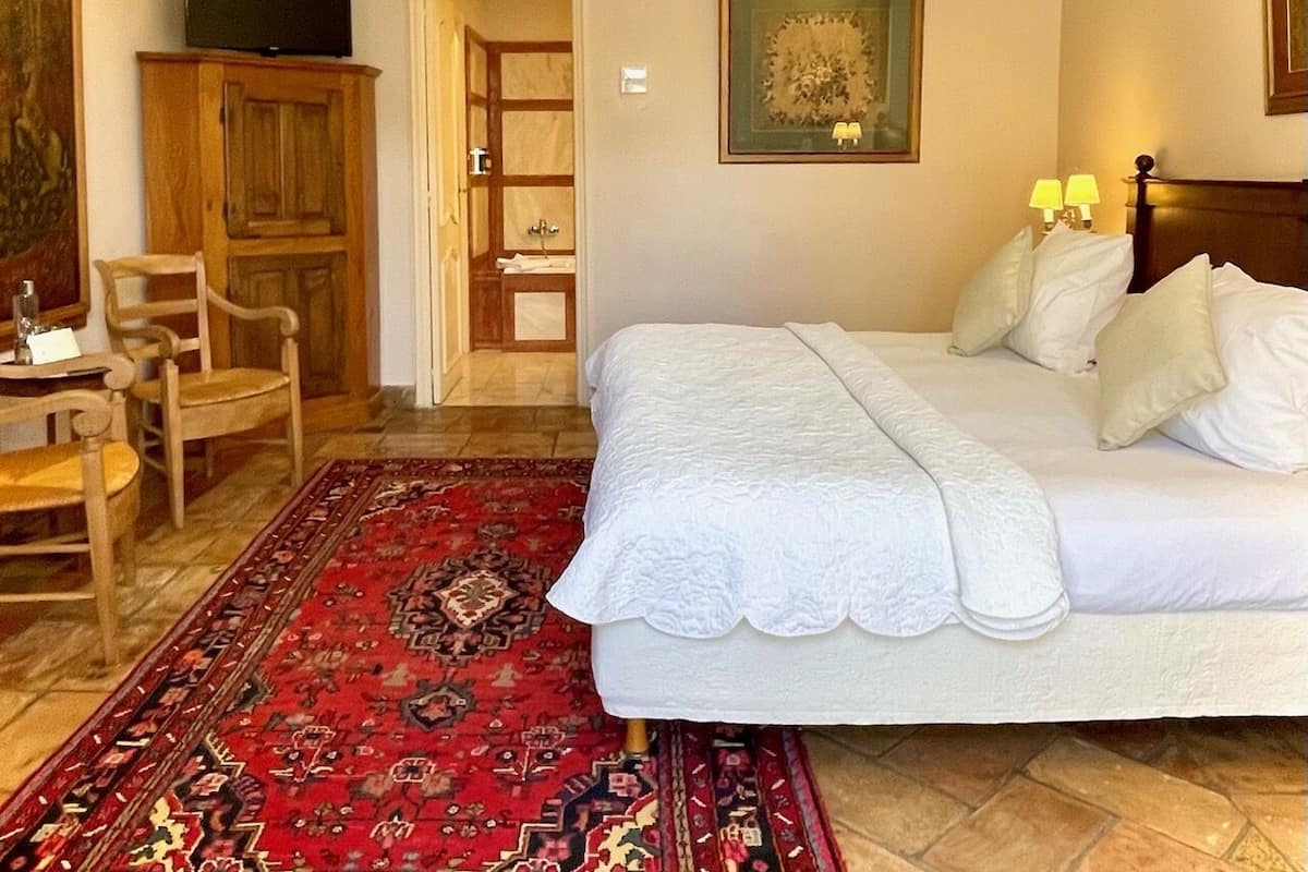 Un dormitorio con una cama, un tapete rojo estampado, un armario de madera, una televisión y un cuadro en la pared.