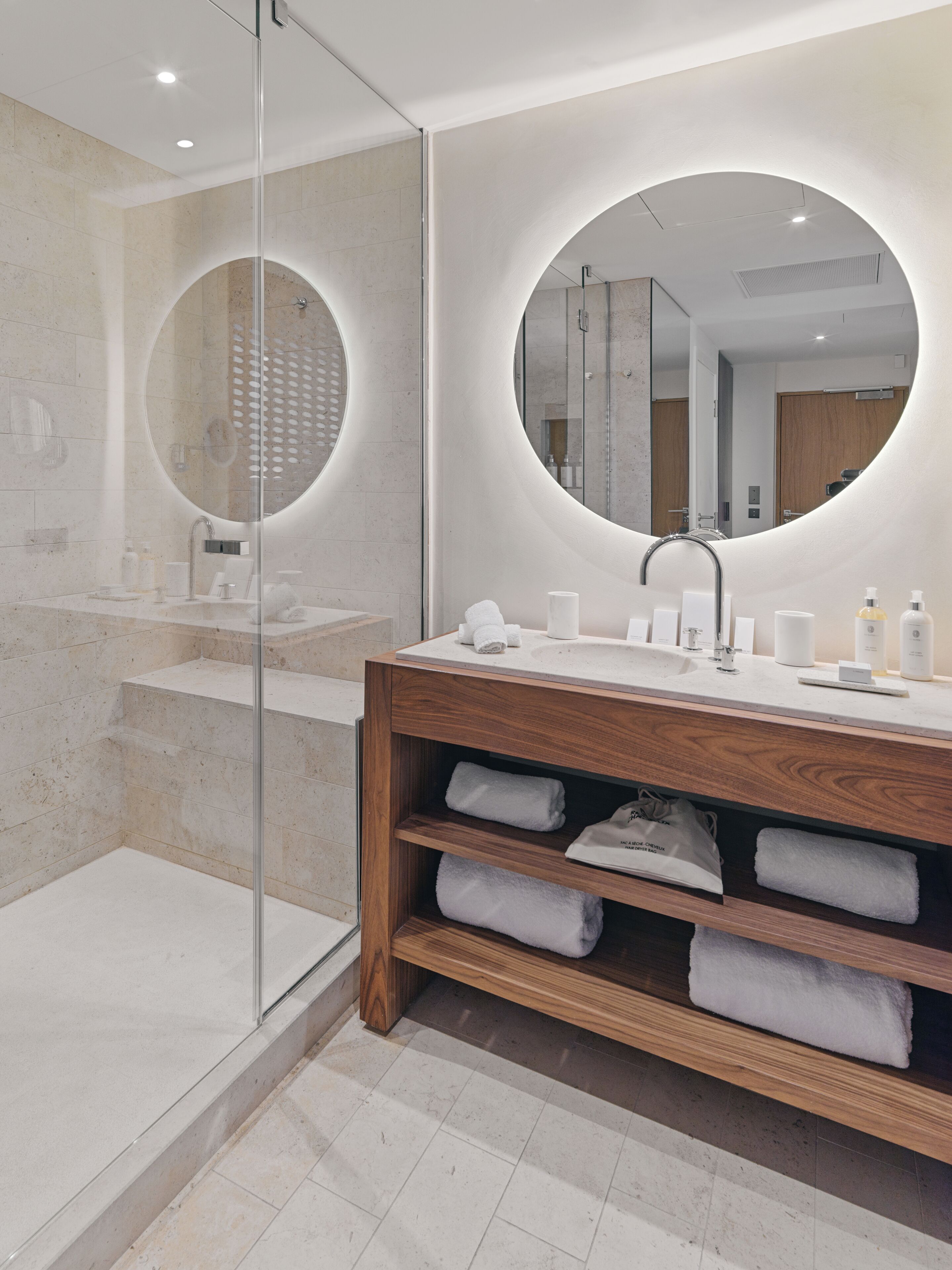 A modern bathroom with a glass-enclosed shower, a wooden vanity with a large mirror, and neatly folded towels.